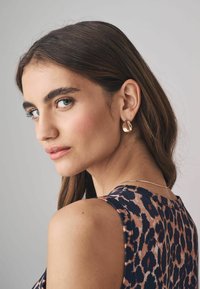 Orecchini a goccia dorati con finitura lucida, abbinati a un top senza maniche con un motivo a stampa leopardata multicolore.