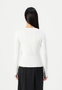 Vit långärmad topp med ribbad textur och scalloped fåll. Ljusskyddad med en flödig svart kjol som framhäver en figursydd silhuett.