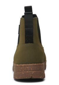 Botín de tobillo verde y negro con material texturizado, que presenta una amplia banda elástica y una suela de goma marrón moteada.