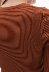 Jersey acanalado de color óxido que presenta una textura de tejido apretado, cuello redondo clásico y costuras a lo largo de los hombros.