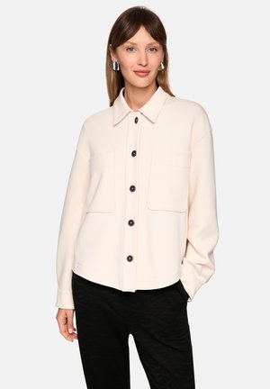 Hellrosa Jacke zum Zumachen mit Kragen, zwei Brusttaschen und schwarzen Knöpfen. Weicher Stoff, lockere Passform und lange Ärmel.