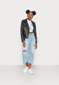 Jaqueta de couro preta com acabamentos em prata, top cropped azul com padrão, jeans largos rasgados em azul claro e ténis brancos.