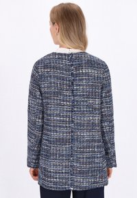Blauwe en witte textuurjack met een losse pasvorm, voorzien van een naad aan de achterkant en lange mouwen. Gemaakt van geweven stof, heeft een klassiek ontwerp.