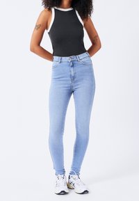 Wysokocięte, jasnoniebieskie rurki jeansowe z denimu, cechujące się gładką fakturą i ponadczasowym designem, zestawione z czarnym, bezrękawnym topem.