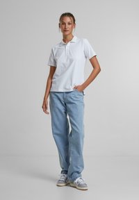 Hvit polo skjorte med kortermet, myk bomullsstoff. Kombinert med lyseblå vide jeans og grå sneakers med hvite detaljer.