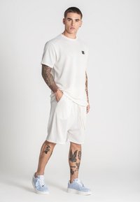 Weißes, strukturiertes T-Shirt und Shorts-Set in lässiger Passform, kombiniert mit hellblauen Sneakern mit Musterdesign.