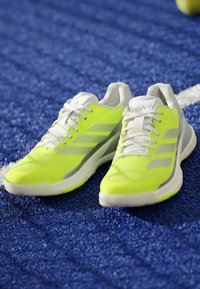 Bright yellow and white athletic shoes with laces placed on a blue textured sports surface near a white line.