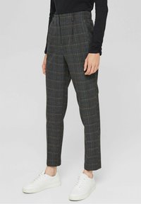 Grijze geruite broek van gestructureerde stof, met een hoge taille en taps toelopende pijpen, gecombineerd met witte sneakers.