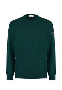 Pullover verde scuro realizzato in tessuto texturizzato, con scollatura rotonda, maniche lunghe e una toppa a forma di triangolo sulla spalla sinistra.