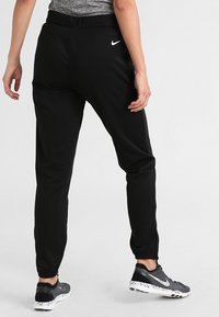 Zwarte sportieve broek met een elastische tailleband en nauwsluitende boorden. Beschikt over een klein wit logo en een gladde, lichte stof.