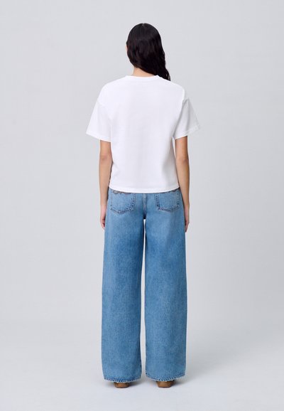 T-shirt bianco in cotone con una vestibilità rilassata, maniche corte e orlo arrotondato, abbinato a jeans in denim a gamba larga di colore blu chiaro con tasche posteriori.