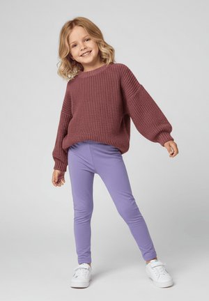Bordowy sweter z dzianiny z dużymi rękawami, zestawiony z dopasowanymi fioletowymi legginsami i białymi trampkami. Gładka faktura i luźny krój.