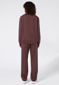 Bruin sporttracksuit met een relaxte pasvorm. Top met lange mouwen en hoge kraag, en bijpassende wijde broek. Glad materiaal en rechte zoom.