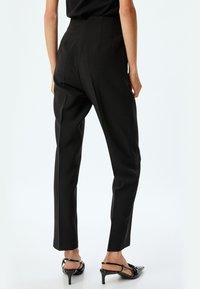 Pantaloni neri su misura con vita alta, caratterizzati da una texture liscia e gambe dritte. Abbinati a sandali neri con tacco.