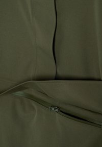Tissu vert olive avec une couture visible et une fermeture éclair partiellement ouverte sur un vêtement, montrant la texture et les détails de la couture.