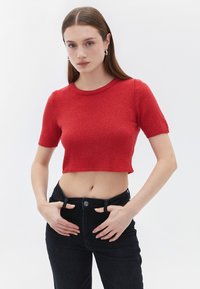 Maglione corto rosso con maniche corte, lavorazione a maglia testurizzata, scollatura rotonda; abbinato a jeans neri a vita alta. Finitura liscia, design aderente.