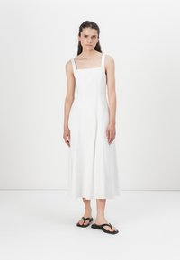 Robe blanche à mi-longueur avec décolleté carré et fines bretelles, fabriquée en tissu léger. Associée à des sandales noires. Texture lisse.