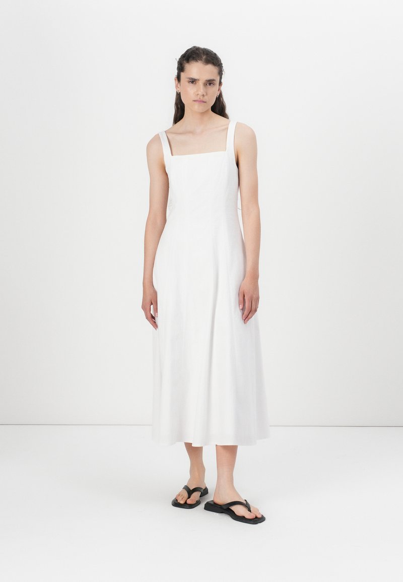 Robe blanche à mi-longueur avec décolleté carré et fines bretelles, fabriquée en tissu léger. Associée à des sandales noires. Texture lisse.