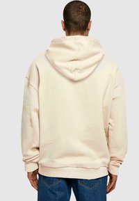 Felpa con cappuccio in beige chiaro, caratterizzata da un fit rilassato, polsini e orlo a costine, con una texture liscia e senza motivi visibili.