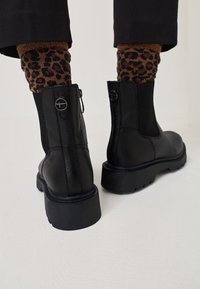 Mustade nahast pahkluu saapad, millel on tahke kummist talla, külgrihm ja elastsed paneelid. Rikkalikult rõhutatud ümmarguste riistade detaljidega.