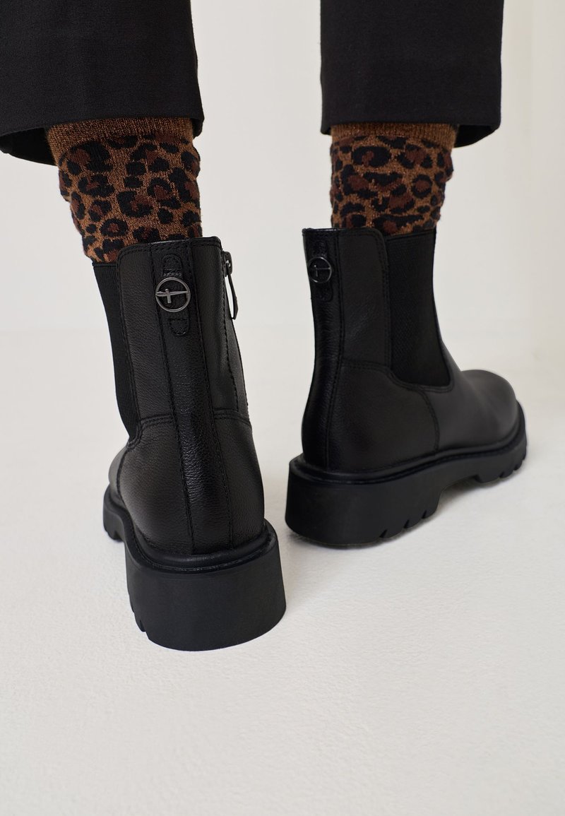 Mustade nahast pahkluu saapad, millel on tahke kummist talla, külgrihm ja elastsed paneelid. Rikkalikult rõhutatud ümmarguste riistade detaljidega.