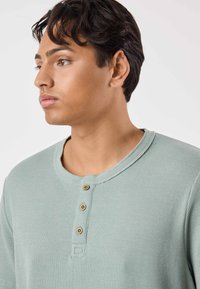 Ljusgrön långärmad henleytröja i texturerat tyg med rund halsringning och tre träknappar vid knappslån.