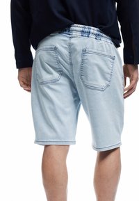 Shorts de mezclilla azul claro con cinturilla elástica, dos bolsillos traseros y detalle de costura en contraste. Textura suave, diseño hasta la rodilla.