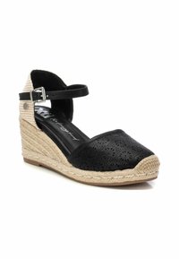 Espadrille de cuña con parte superior de cuero negro perforado, correa en el tobillo y suela de yute trenzado. Presenta un acento textil a cuadros en la parte trasera.