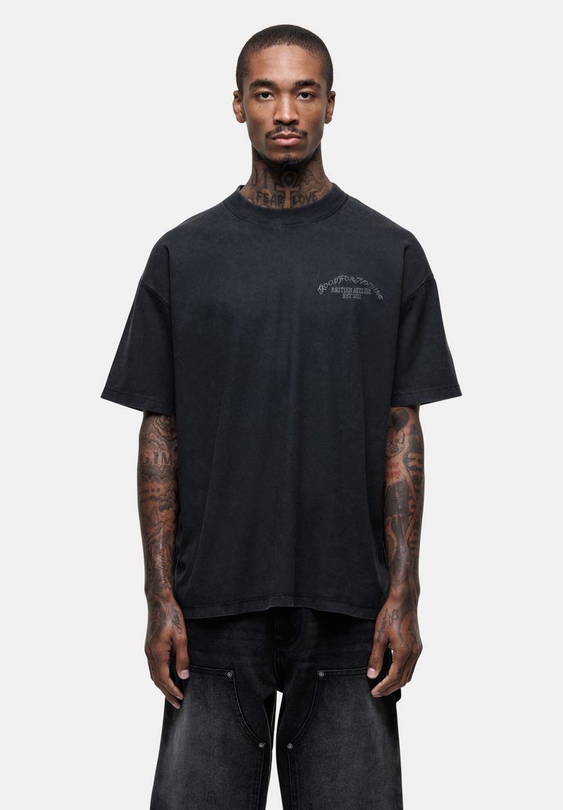 Zwarte oversized t-shirt van zachte katoen, met een ronde hals, korte mouwen en subtiele grafische details aan de voorkant. Geweven stofafwerking.