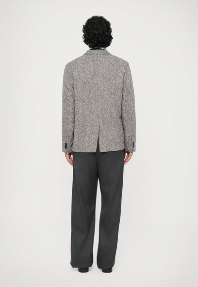 Grå uldblandingsblazer med pyntelapper, enkelt slids bagpå og knapmanchetter, parret med mørkegrå plisserede bukser.