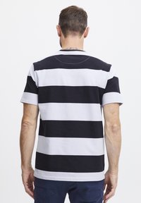 Melna un balta svītraina īsās piedurknes T-kreklā, kas izgatavots no kokvilnas, ar apaļu kaklu un brīvu piegriezumu. Redzamais šuvums ap kaklu.