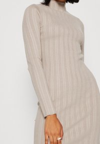 Abito in maglia beige chiaro con colletto alto e maniche lunghe. Presenta una texture a coste verticali e una silhouette aderente. Tessuto morbido ed elastico.