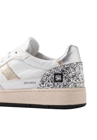 Baskets en cuir blanches avec un talon métal argenté, des accents argentés pailletés, une semelle beige et un design à rayures dorées sur le côté.