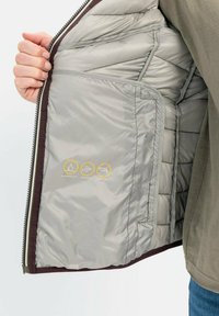 Graue Daunenjacke von innen, die das gesteppten Futter zeigt, mit sichtbaren Etiketten, die wasserabweisende, winddichte und daunenfreie Eigenschaften anzeigen.