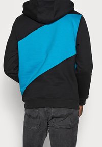 Mikina s kapucí s diagonálním černoblavým designem, vyrobená z měkké tkaniny s hladkou texturou. Obsahuje žebrované manžety a lem.