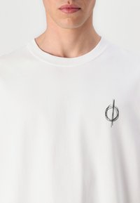 White cotton t-shirt with a round neck; features a minimalist black graphic design on the left side. Soft texture, standard fit.