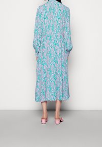 Robe longue et ample en tissu léger avec un motif abstrait turquoise et rose. Manches ballons et coupe droite. Sandales à talons blocs roses.