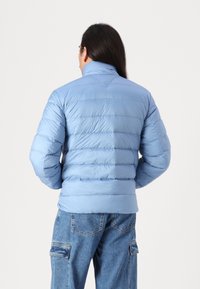 Ljusblå puffjacka med hög krage och horisontell sömnad. Har en slät, glänsande yta och en avslappnad passform. I kombination med jeans.