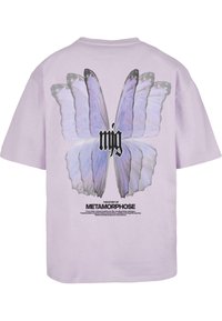 Lilla t-shirt med korte ærmer, der har et stort sommerfugle motiv på ryggen, med sort tekst der står "mjg" og "BERETNINGEN OM METAMORFOSE" nedenunder.