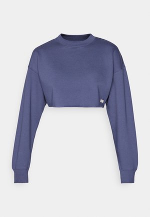 Cropped purple sweatshirt with long sleeves, round neck, and ribbed cuffs. Features a small logo tag on the hem. Smooth texture.