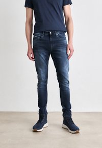 Mörkblå smala jeans med en blekt design och femficksstil, kombinerade med marinblå sneakers. Bomullsmaterial med lätt stretch.
