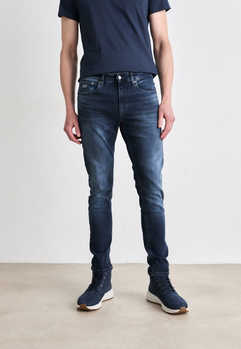 Mörkblå smala jeans med en blekt design och femficksstil, kombinerade med marinblå sneakers. Bomullsmaterial med lätt stretch.