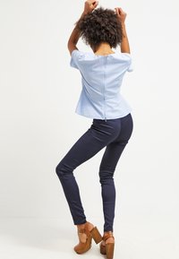 Ljusblå kortärmad peplumtop med en dragkedja i centrum bak, i kombination med marinblå slim-fit byxor och bruna platåsandaler.