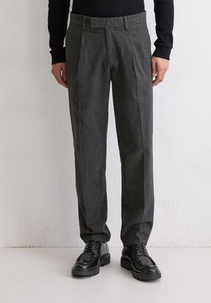 Grijze wollen broek met een getailleerde pasvorm, voorzien van een vlakke voorkant, dubbele plooien en een gladde textuur. Gecombineerd met zwarte veterschoenen.