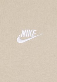 Logo Nike blanc brodé avec swoosh sur fond de tissu beige texturé.