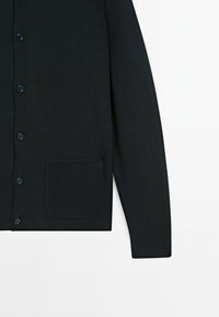 Zwarte cardigan met een geribbelde textuur, knoopsluiting en een voorzak. Heeft een aansluitend ontwerp met lange mouwen en subtiele stikseldetails.