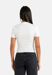 Hvid t-shirt med korte ærmer og rund halsudskæring, tætsiddende design, kombineret med mørke jeans med baglommer og et mærkat.