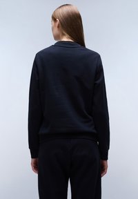 Felpa nera con collo a rondine e polsini a coste. Texture morbida, vestibilità rilassata e design semplice senza loghi o motivi visibili.