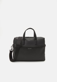 Borsa in pelle nera con texture a ciottoli, doppio manico e tracolla removibile. Presenta una chiusura con zip e il logo Calvin Klein sul fronte.