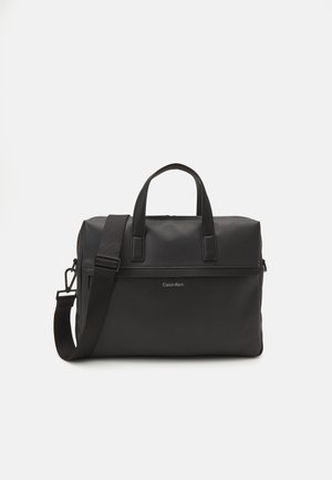 Borsa in pelle nera con texture a ciottoli, doppio manico e tracolla removibile. Presenta una chiusura con zip e il logo Calvin Klein sul fronte.